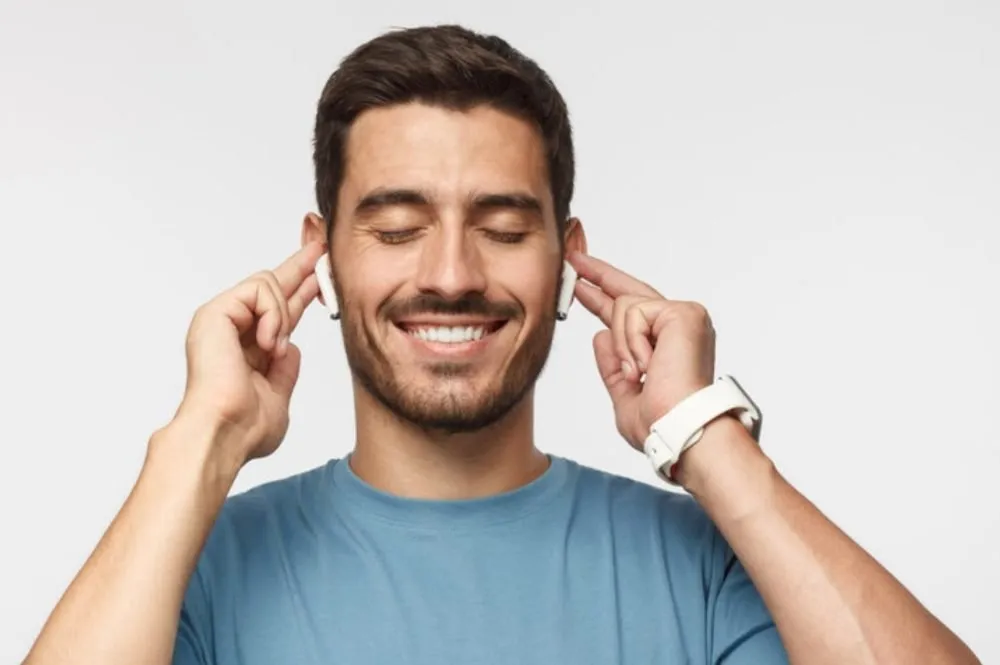Vrolijke man met een brede glimlach, aanrakend en genietend van draadloze oordopjes terwijl hij naar muziek luistert.