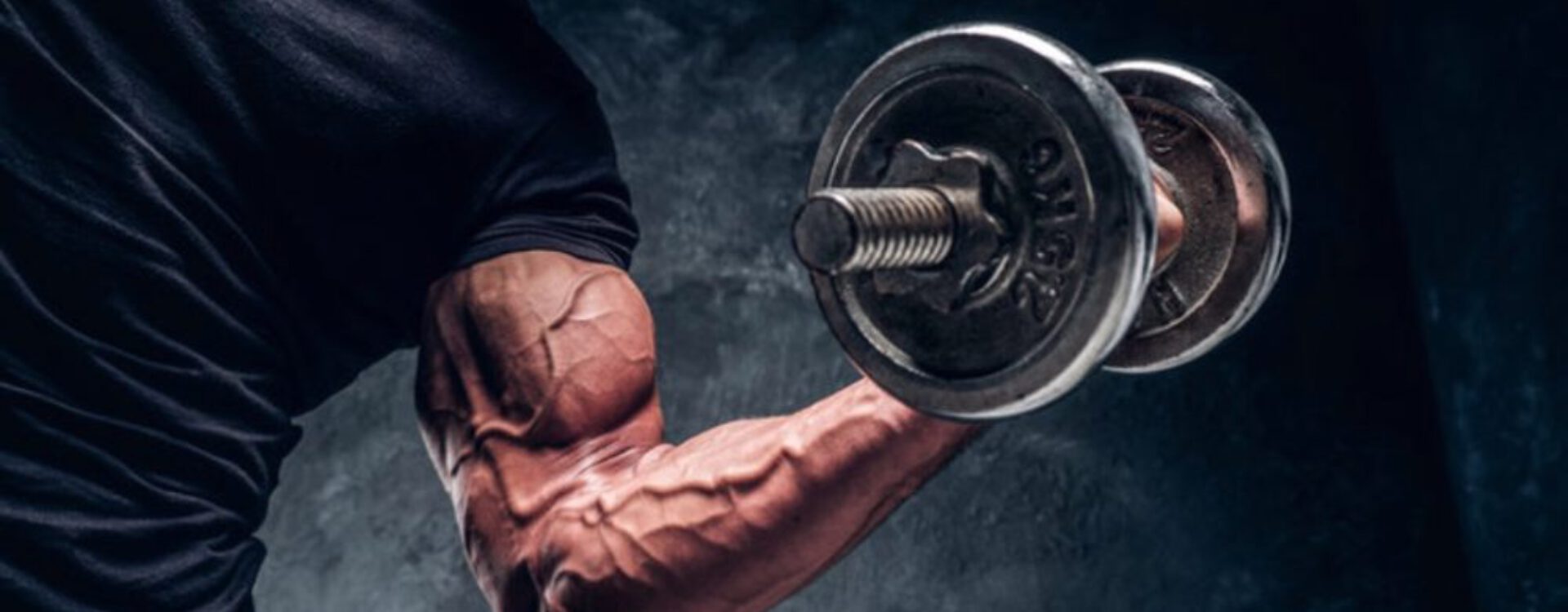 Een gespierde man met een halterschijf in zijn hand, terwijl zijn gespierde arm en torso goed zichtbaar zijn tijdens het uitvoeren van een fitnessoefening.